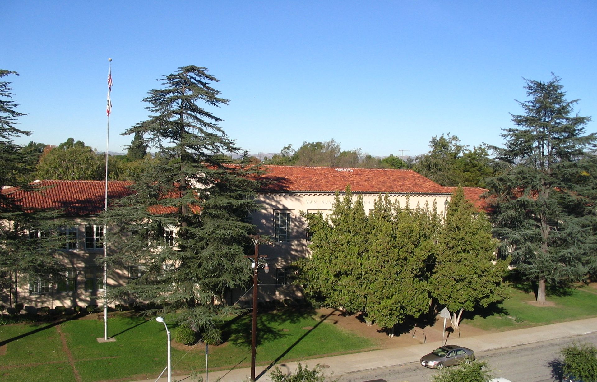 A large building with a red tile roof is surrounded by trees