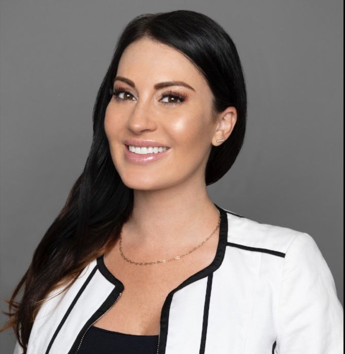 A woman wearing a white jacket and black top smiles for the camera