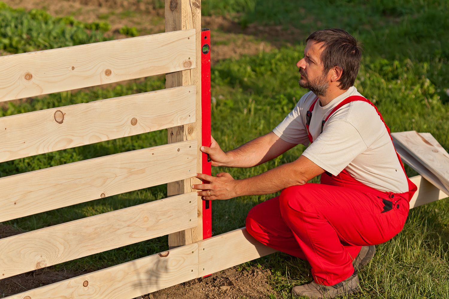 A worker installing a wooden privacy fence in a commercial property. A worker installing a wooden privacy fence in a commercial property.