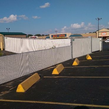 Chain-link fence with white screening in a parking lot in front of a Big Lots store and other businesses.