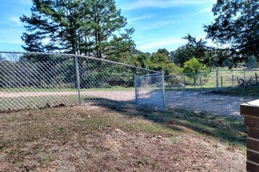 Black chain-link fence, bordering wooden fence, on green grass, with trees in background.