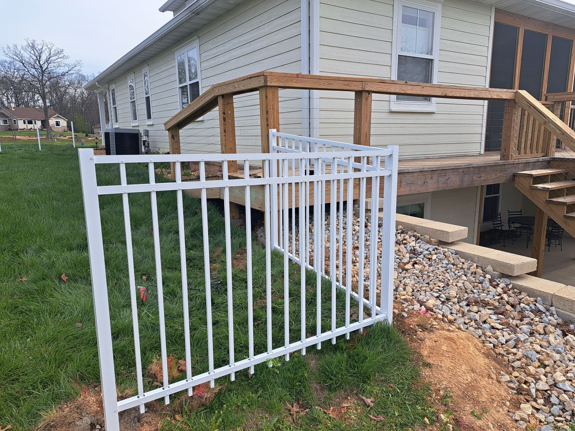 White metal accessibility ramp and stairs leading to a house with a wooden deck and gravel path