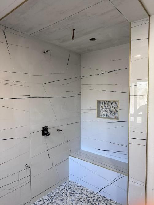 A bathroom with white tiles and a bench in the shower.