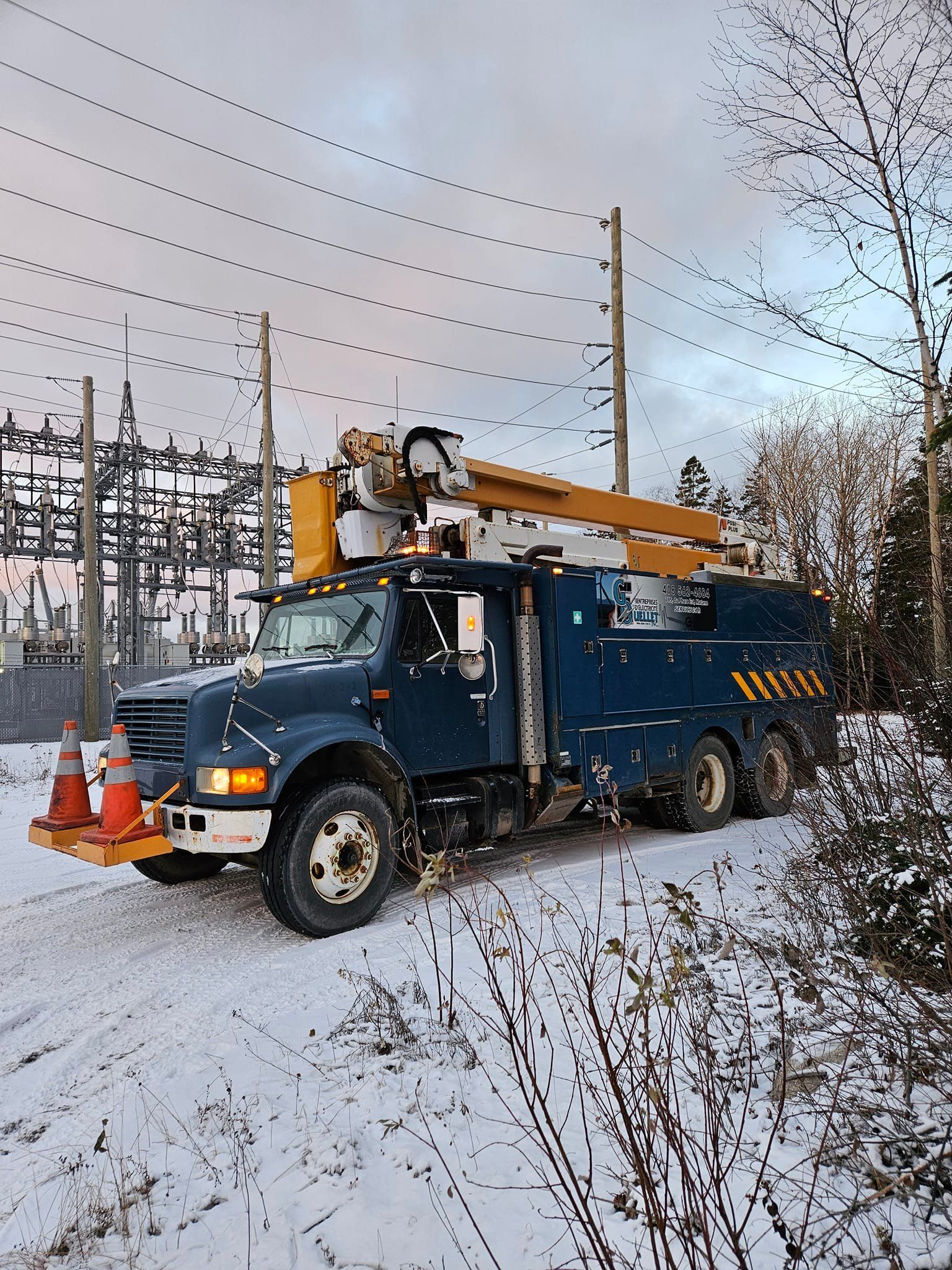 Un camion bleu avec une grue dessus est garé dans la neige.