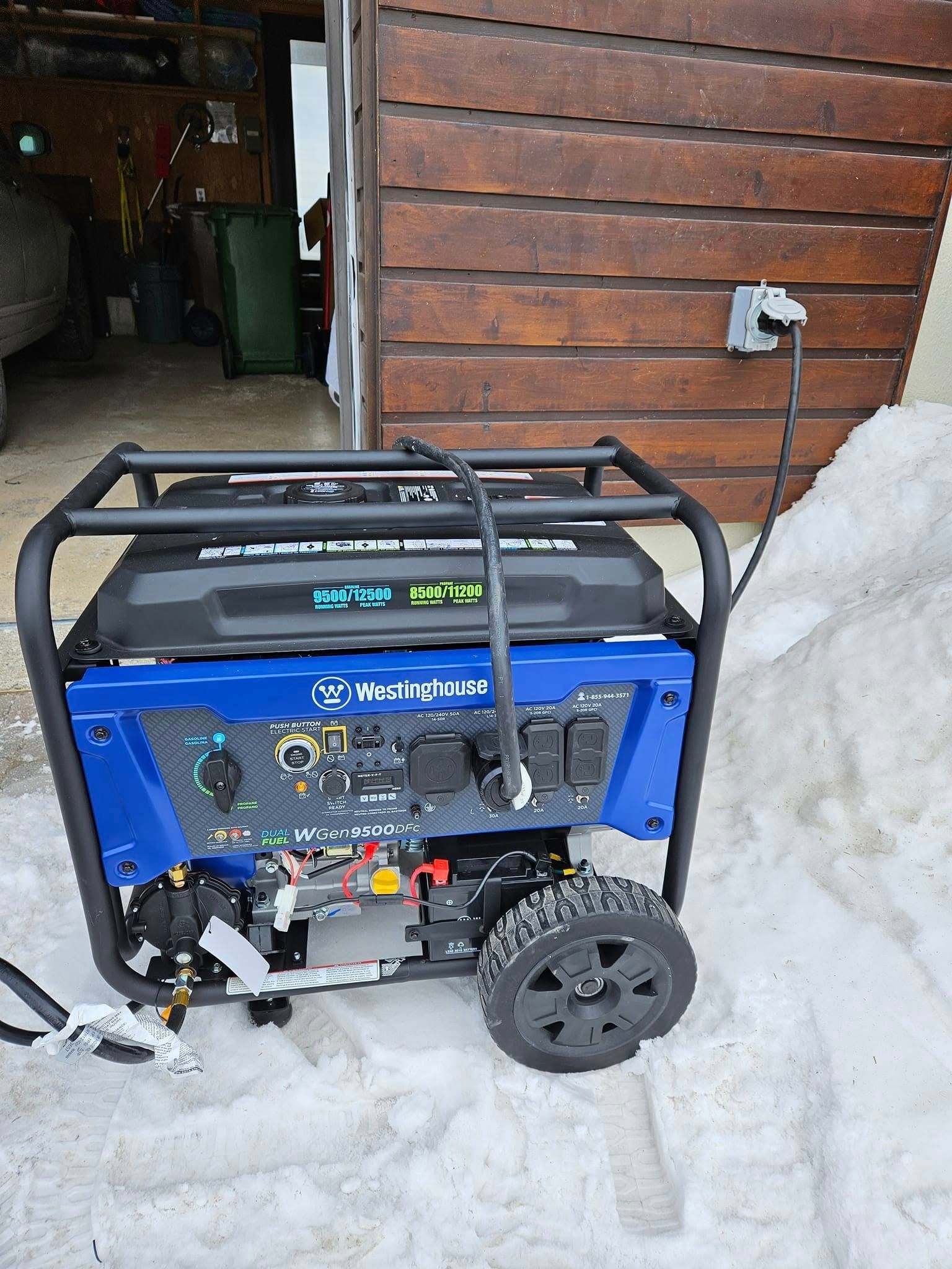 Un générateur est assis dans la neige devant un bâtiment en bois.
