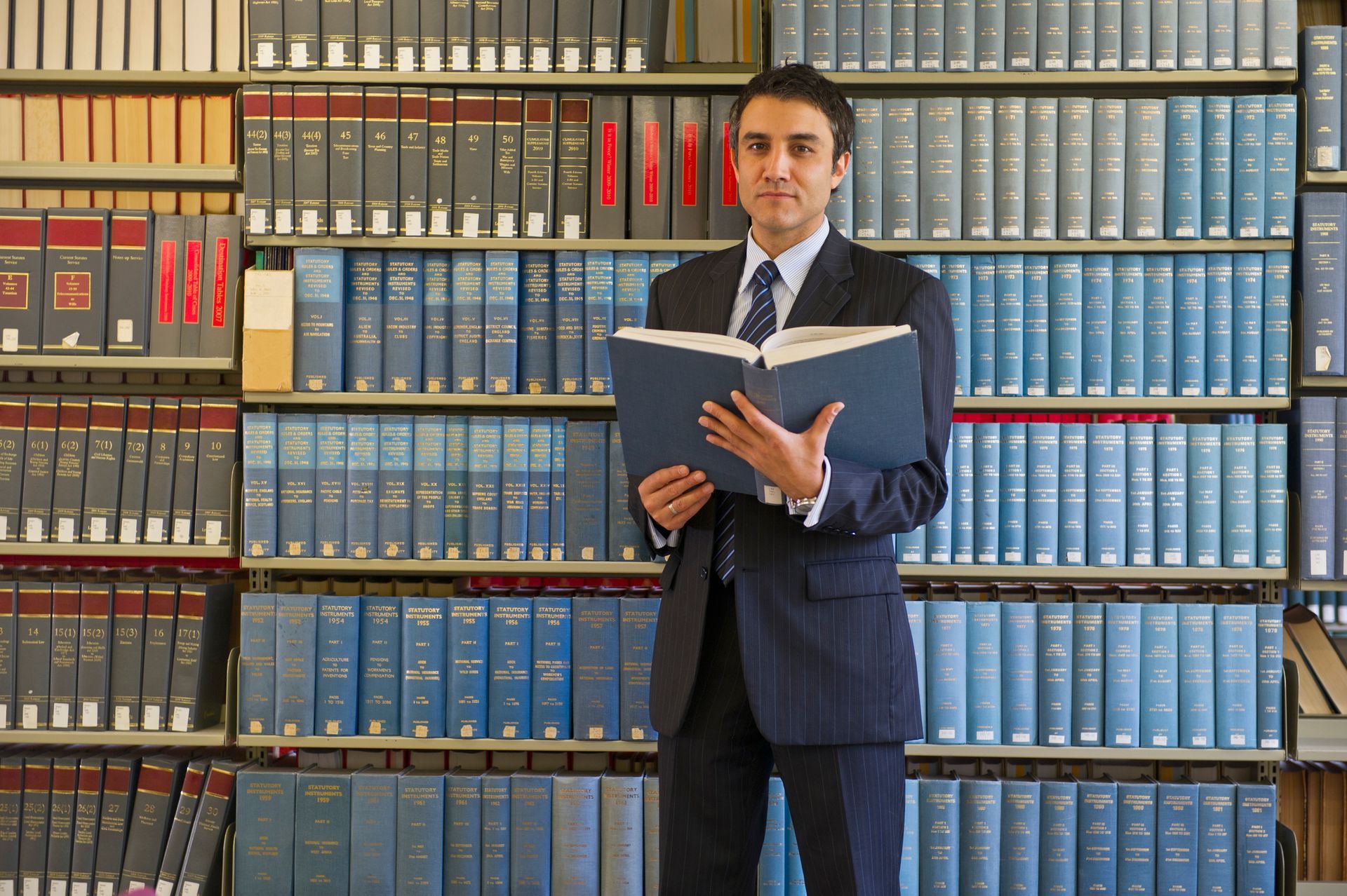 A man in a suit is reading a book in a library.
