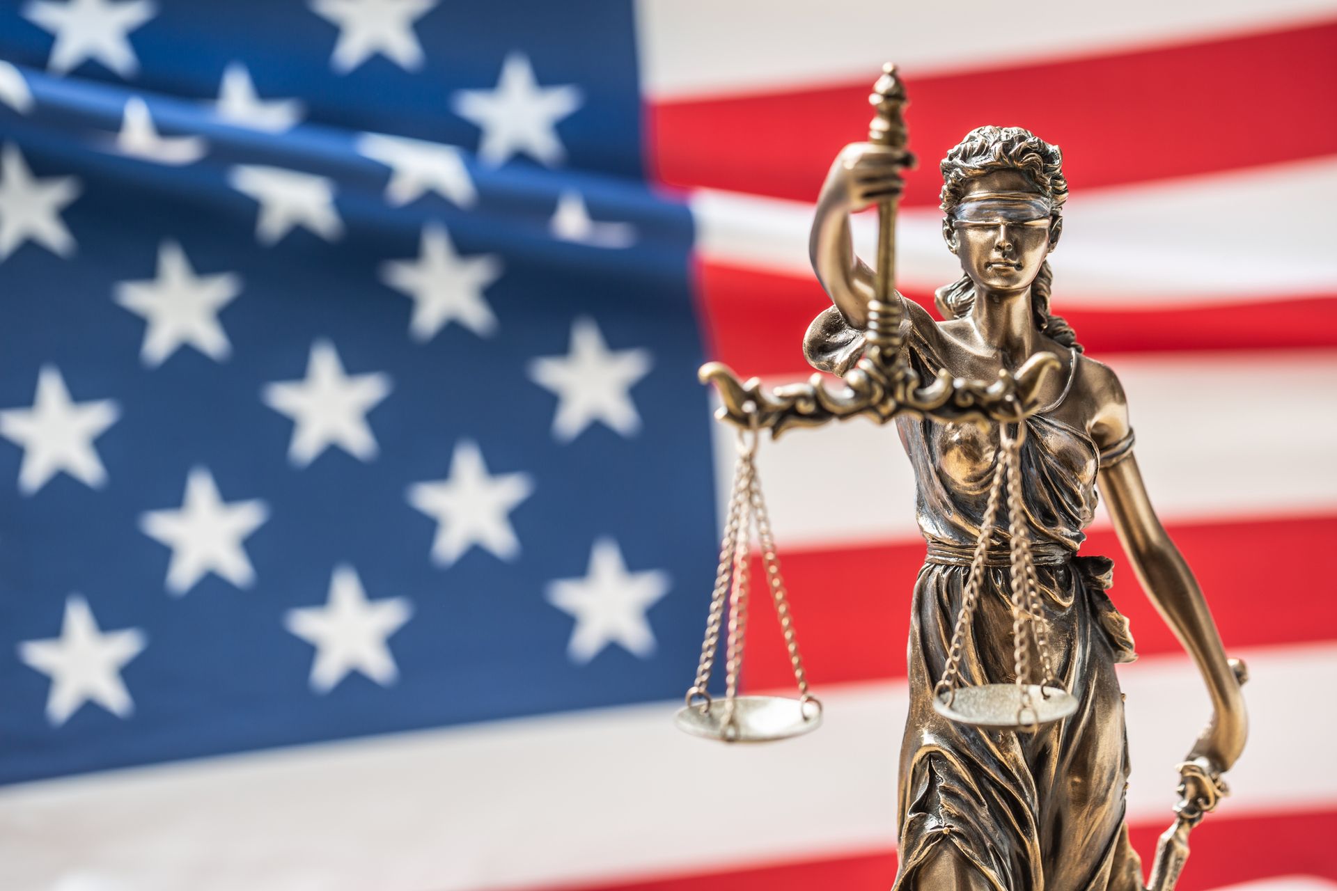 A statue of justice holding scales in front of an American flag.