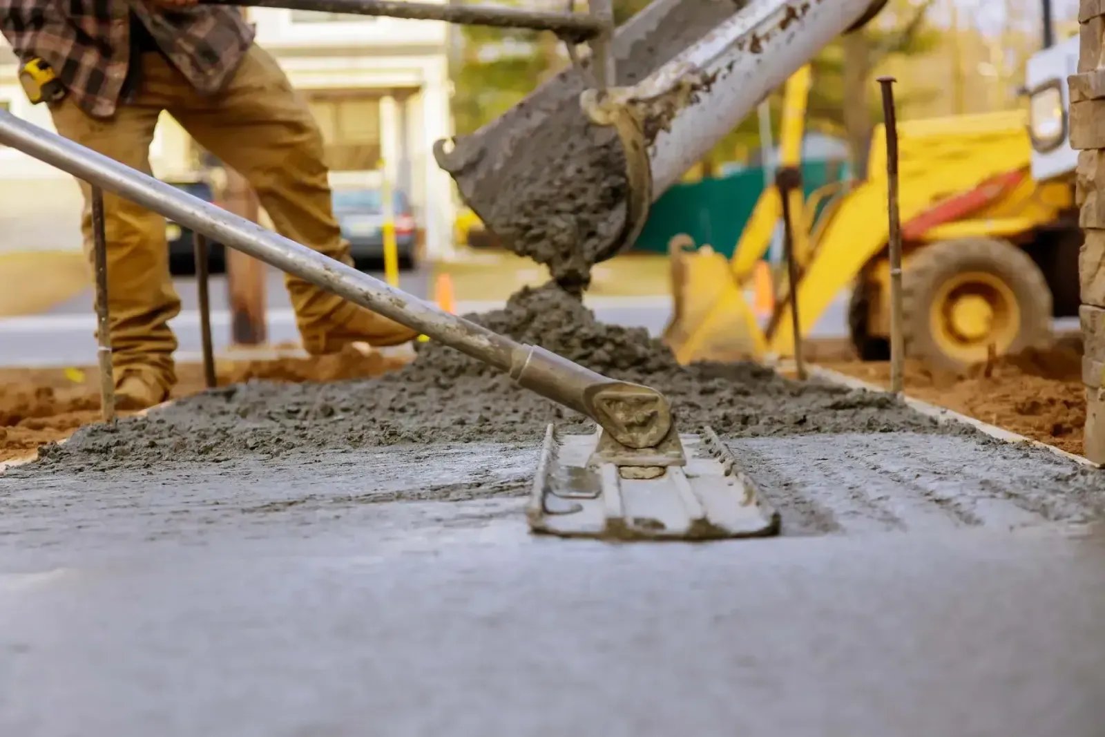 A man is spreading concrete on a sidewalk with a rake.