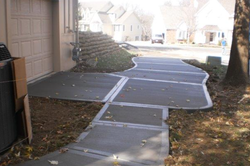 a concrete walkway leading to a garage with houses in the background