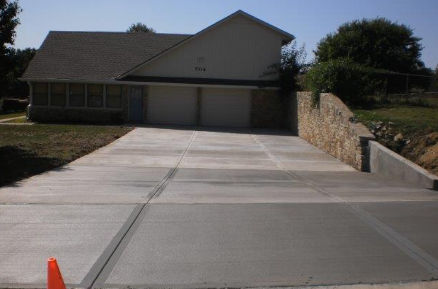 a concrete driveway leading to a house with a stone wall