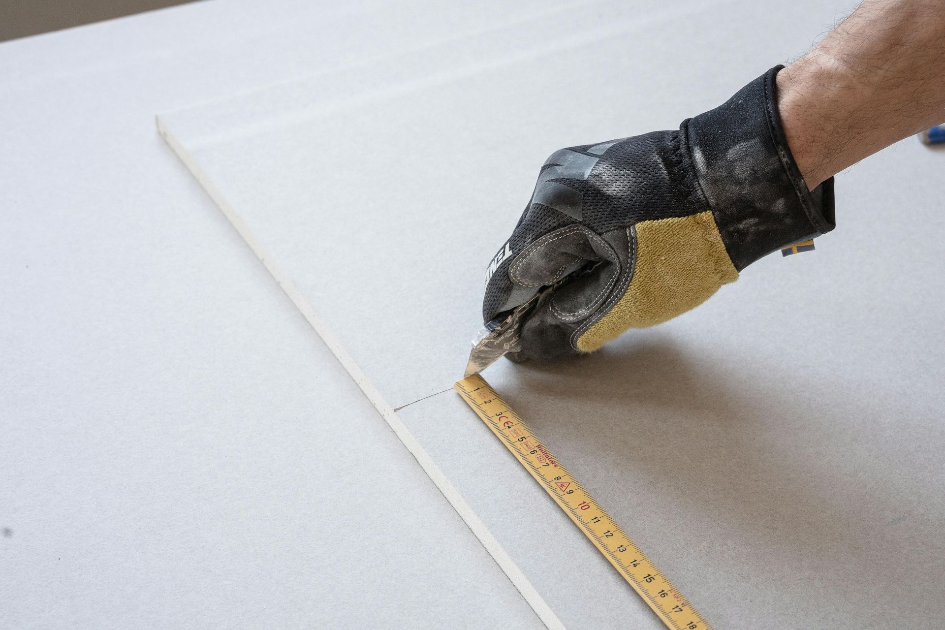 A person is measuring a piece of drywall with a tape measure.