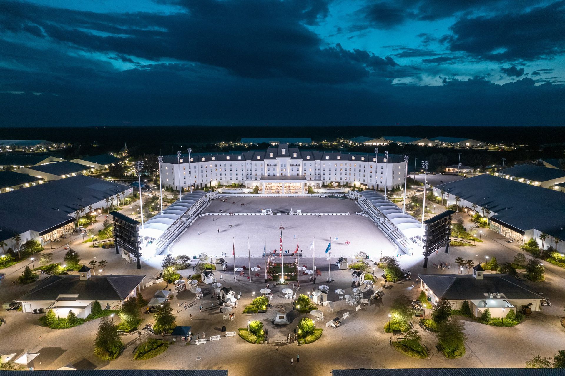 Nighttime aerial view of a large equestrian arena, white building, and surrounding illuminated grounds.