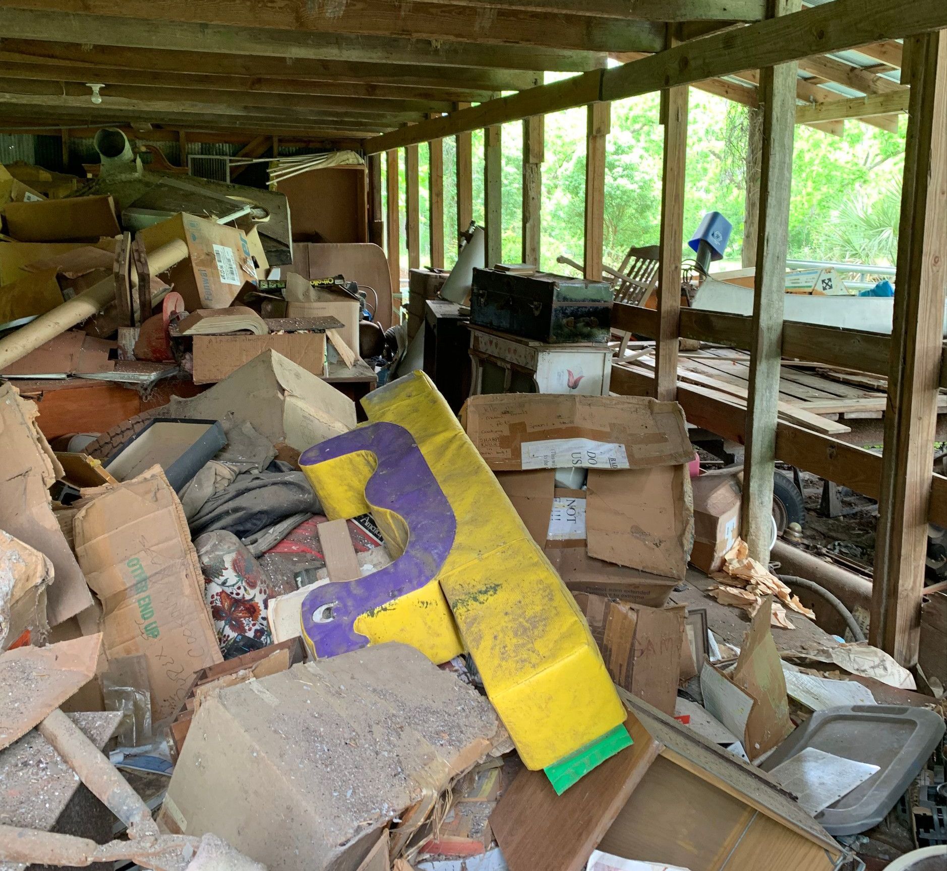 Messy storage shed filled with cardboard boxes, debris, and a partially visible yellow and purple object.