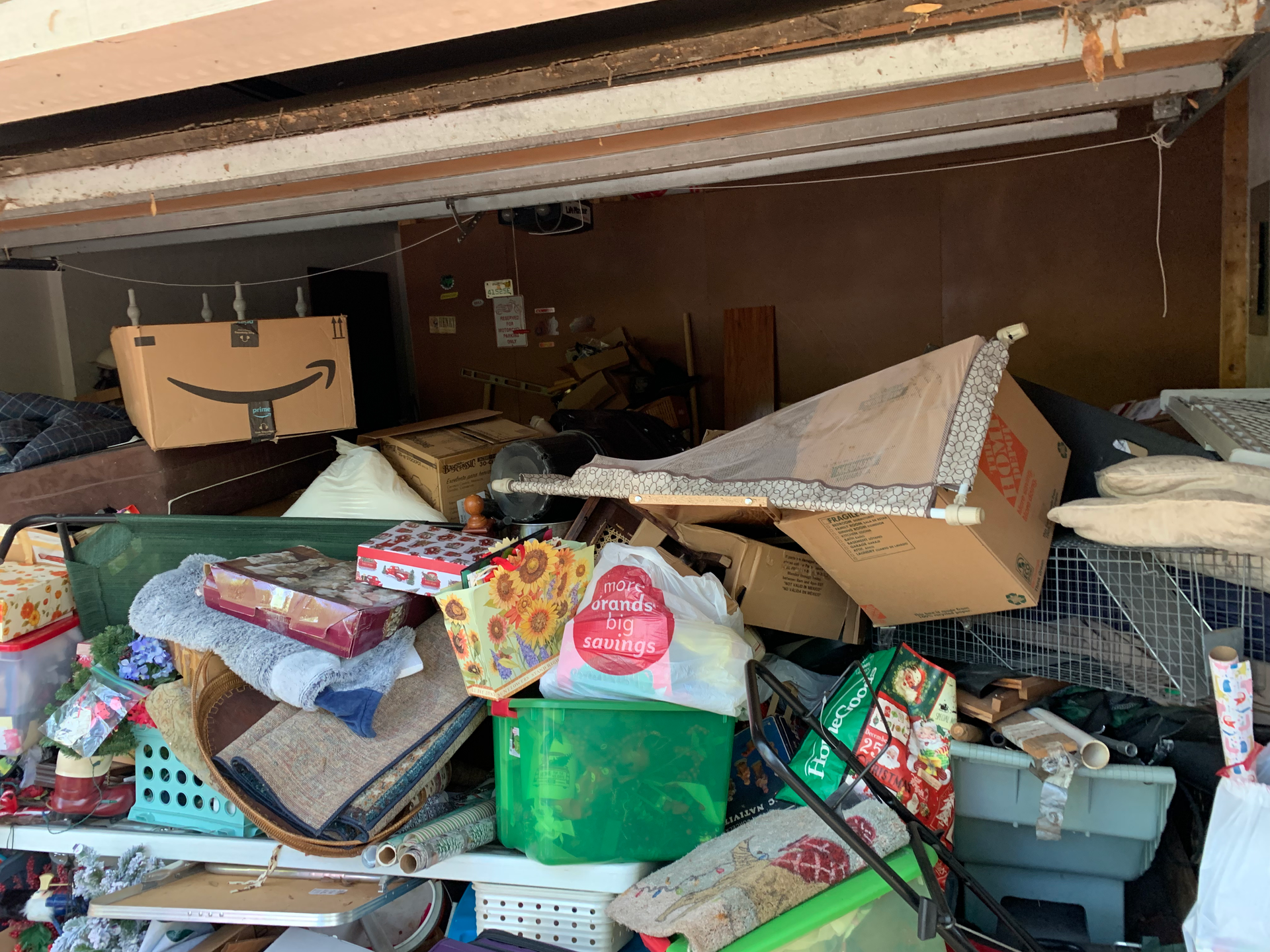 Cluttered garage interior. Various boxes, bags, and items piled up. Amazon box visible.