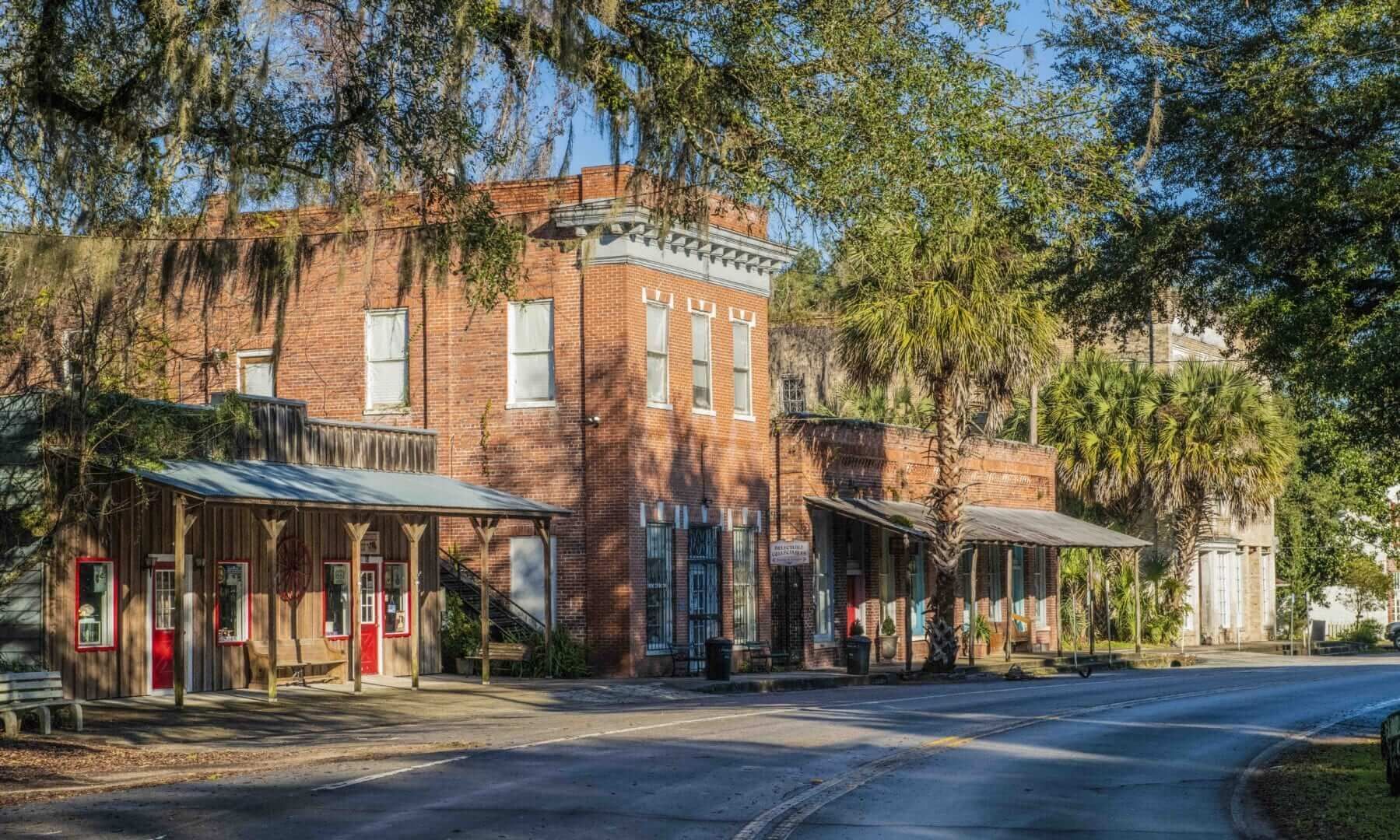 Red brick buildings with awnings line a road, framed by trees.