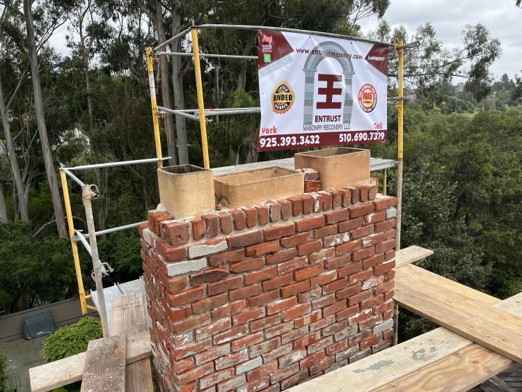 Brick chimney under construction with scaffolding and company sign.