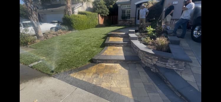 Steps leading up to a house with a green lawn and two men standing near the driveway.