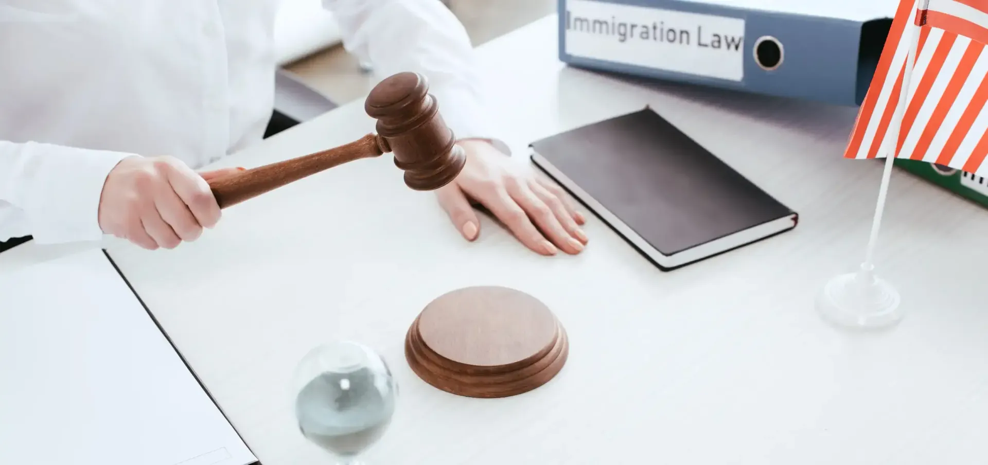 Judge’s gavel on a white desk with law books, a tablet, and a small U.S. flag