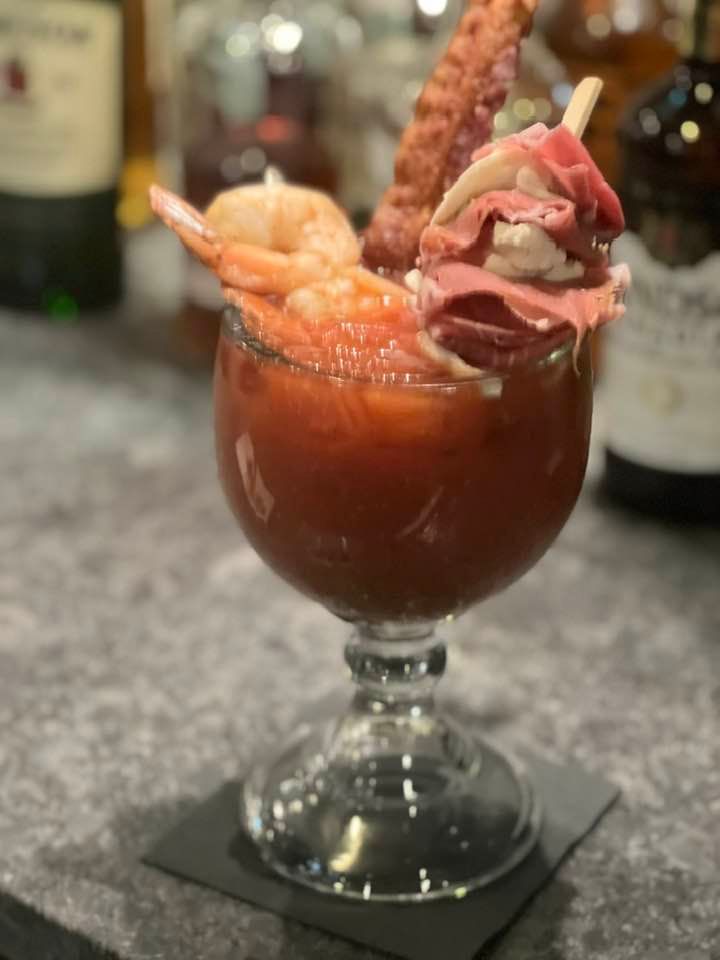 Bloody Mary cocktail with shrimp and bacon garnish in a stemmed glass on a bar counter