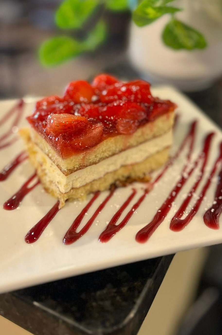 Slice of layered strawberry cake on a white plate with berry sauce drizzle