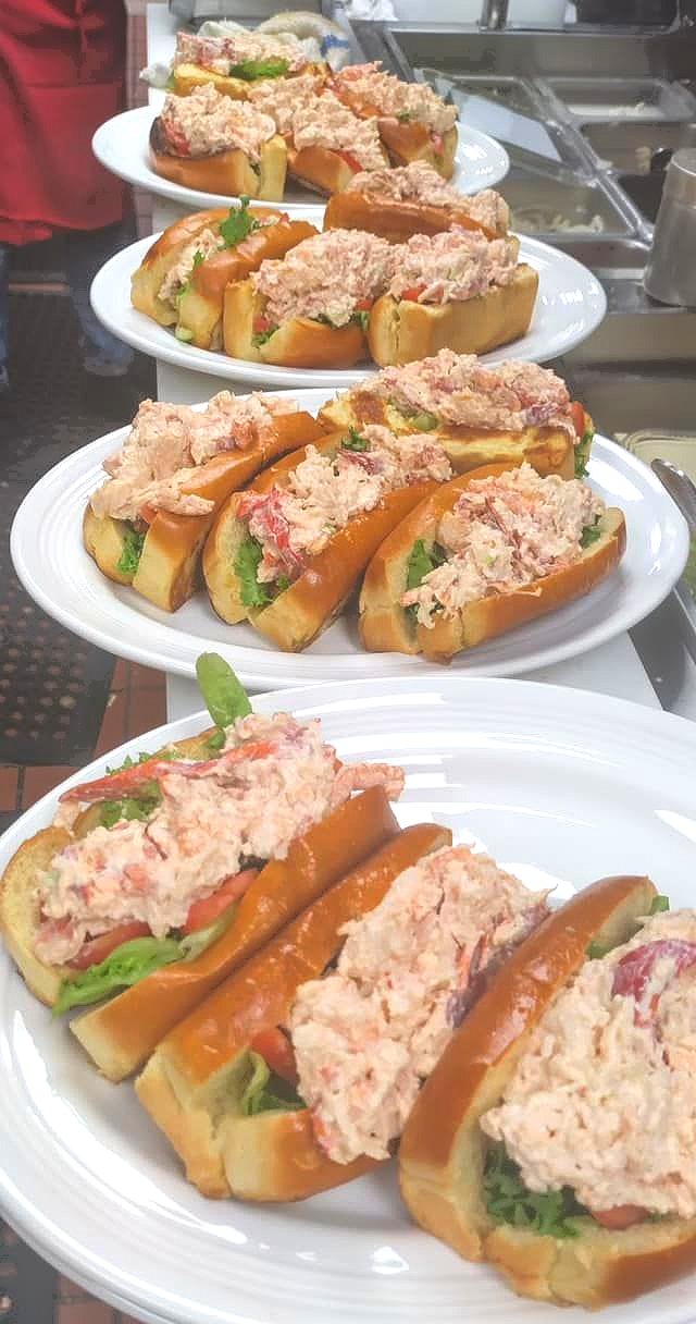 Plates of lobster rolls arranged on a counter, topped with creamy filling and garnished with herbs