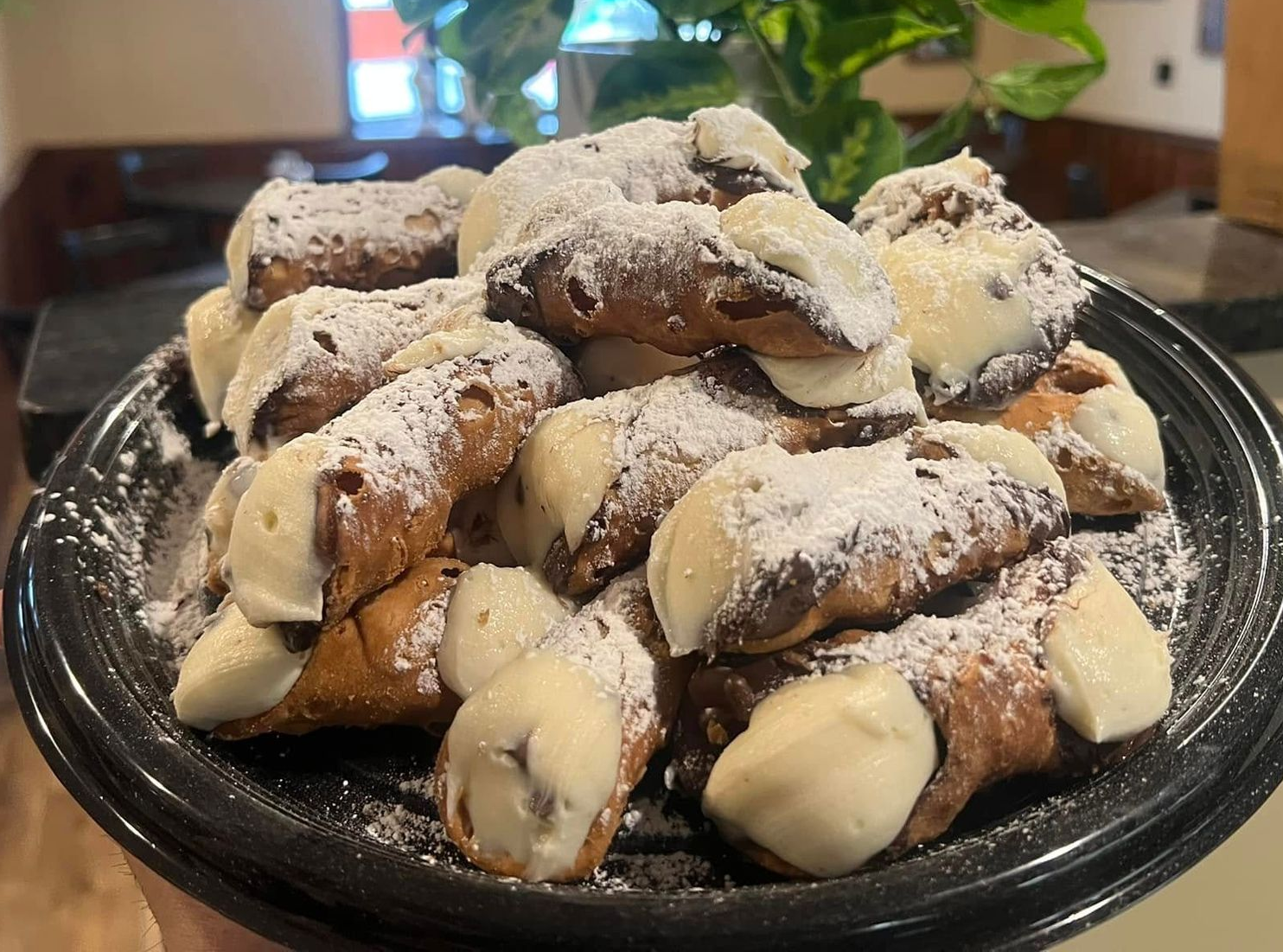Plate of powdered cannoli with cream filling on a black platter, in a dining setting