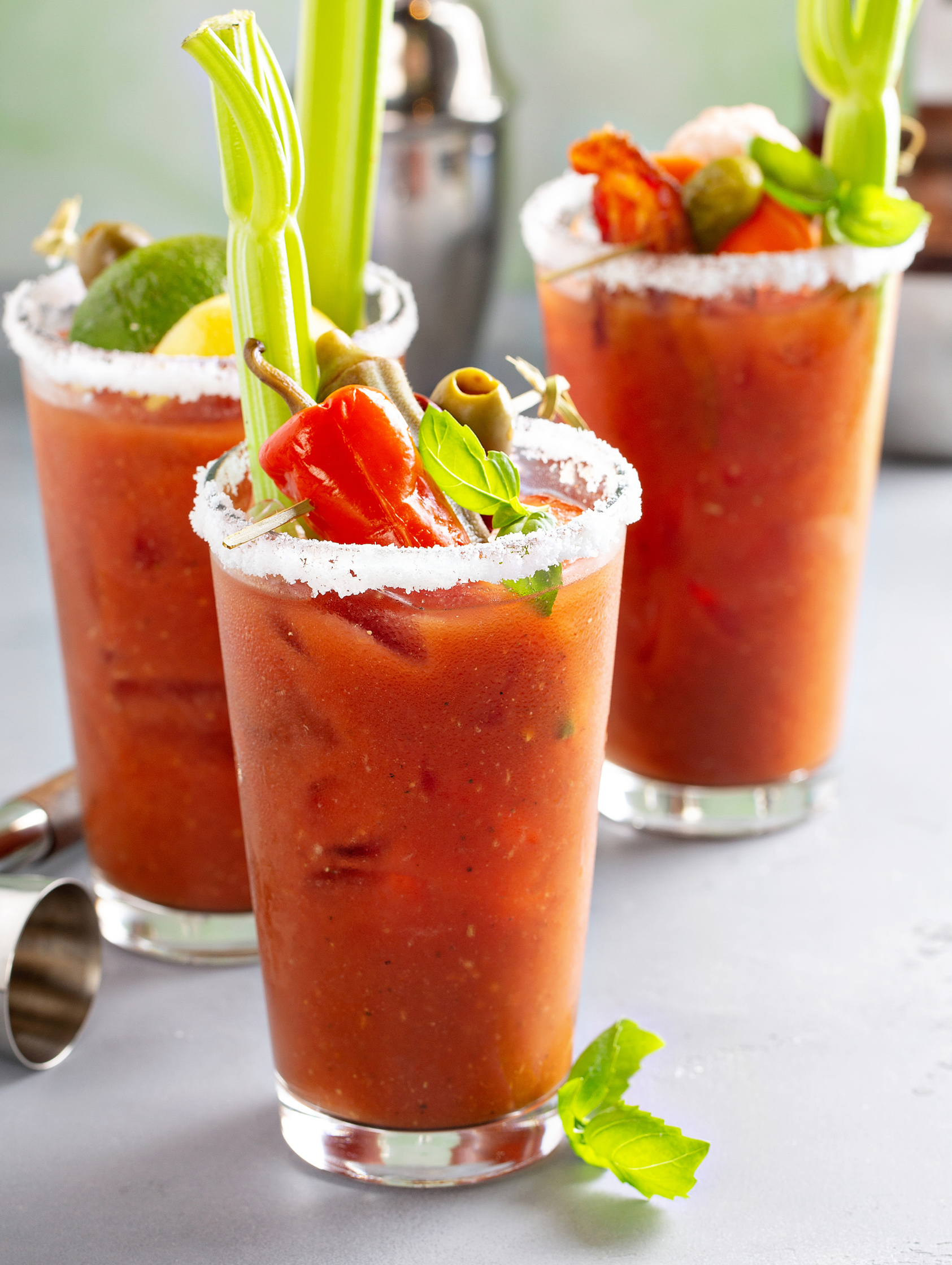 Three strawberry cocktails topped with celery and fruit on a table