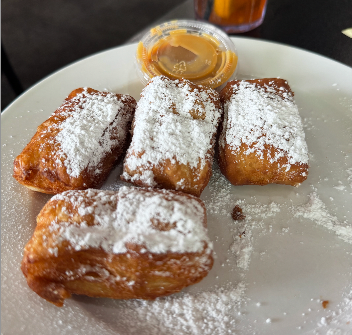 Powdered sugar-dusted fried pastries on a white plate with caramel sauce