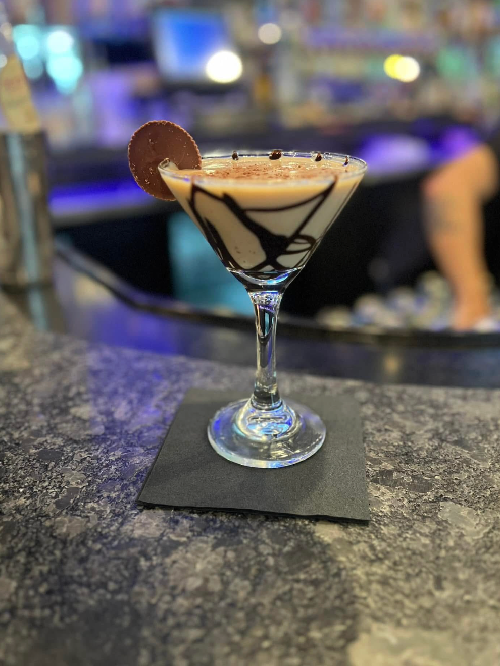 Cocktail in a martini glass with chocolate drizzle and a cookie garnish on a bar counter