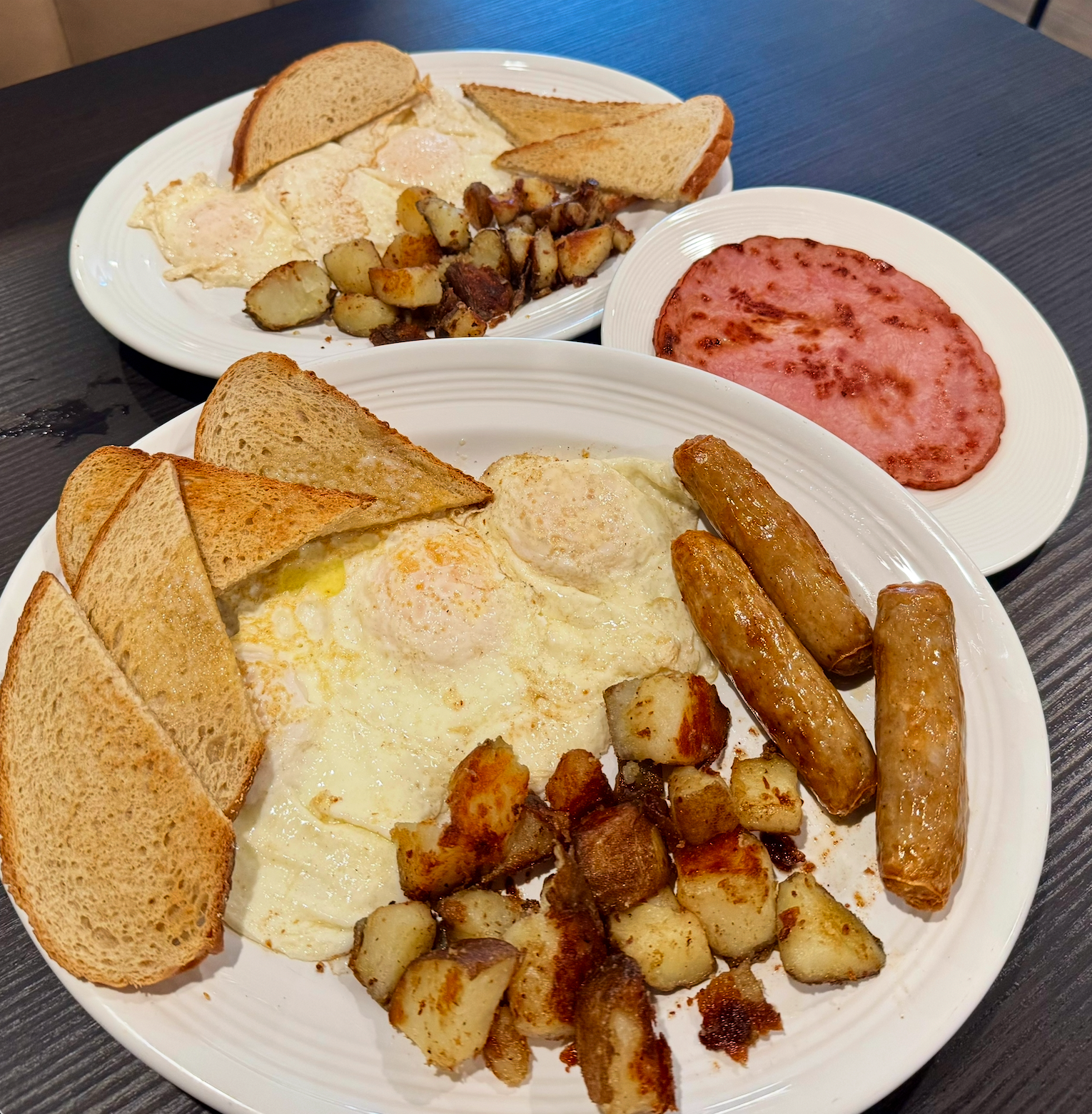 Two plates of breakfast with eggs, toast, potatoes, sausage, and a side of pink jam