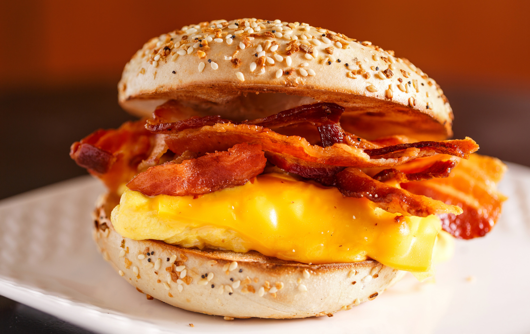 Bacon and melted cheese breakfast sandwich on a sesame bun on a white plate