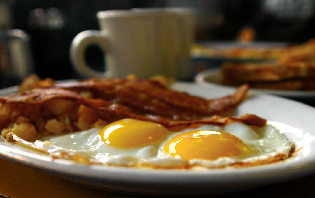 Bacon and two sunny-side-up eggs on a plate with a coffee cup in the background