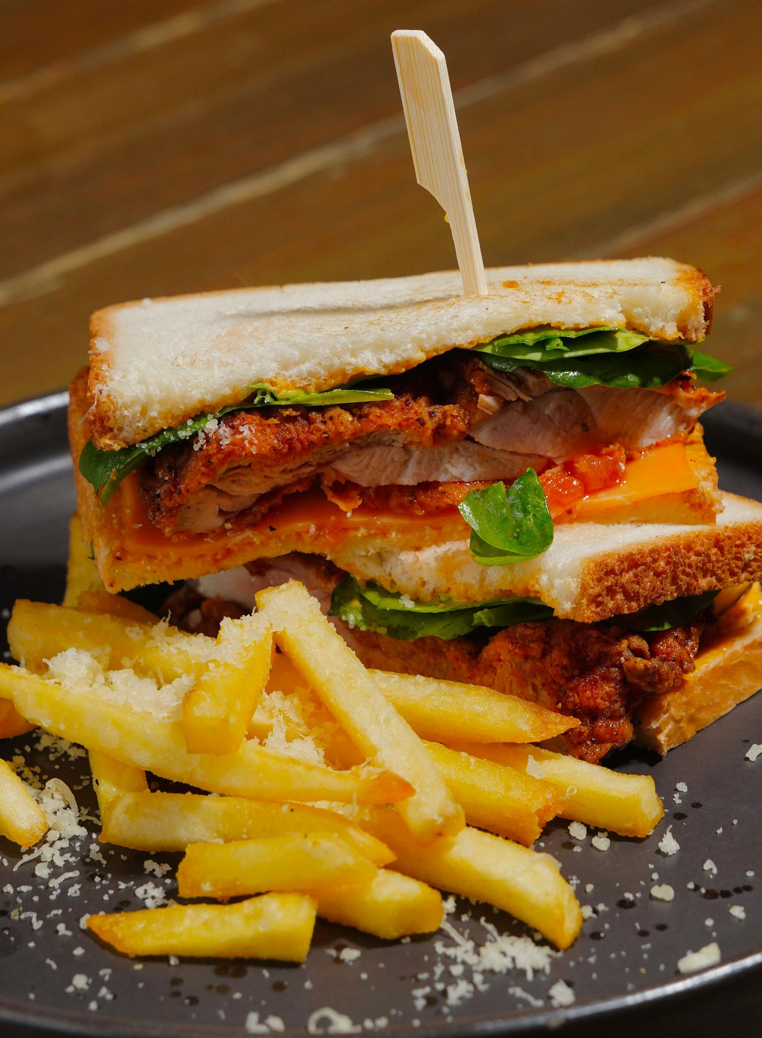 Club sandwich with fries on a black plate, stacked with lettuce, tomato, and bacon.