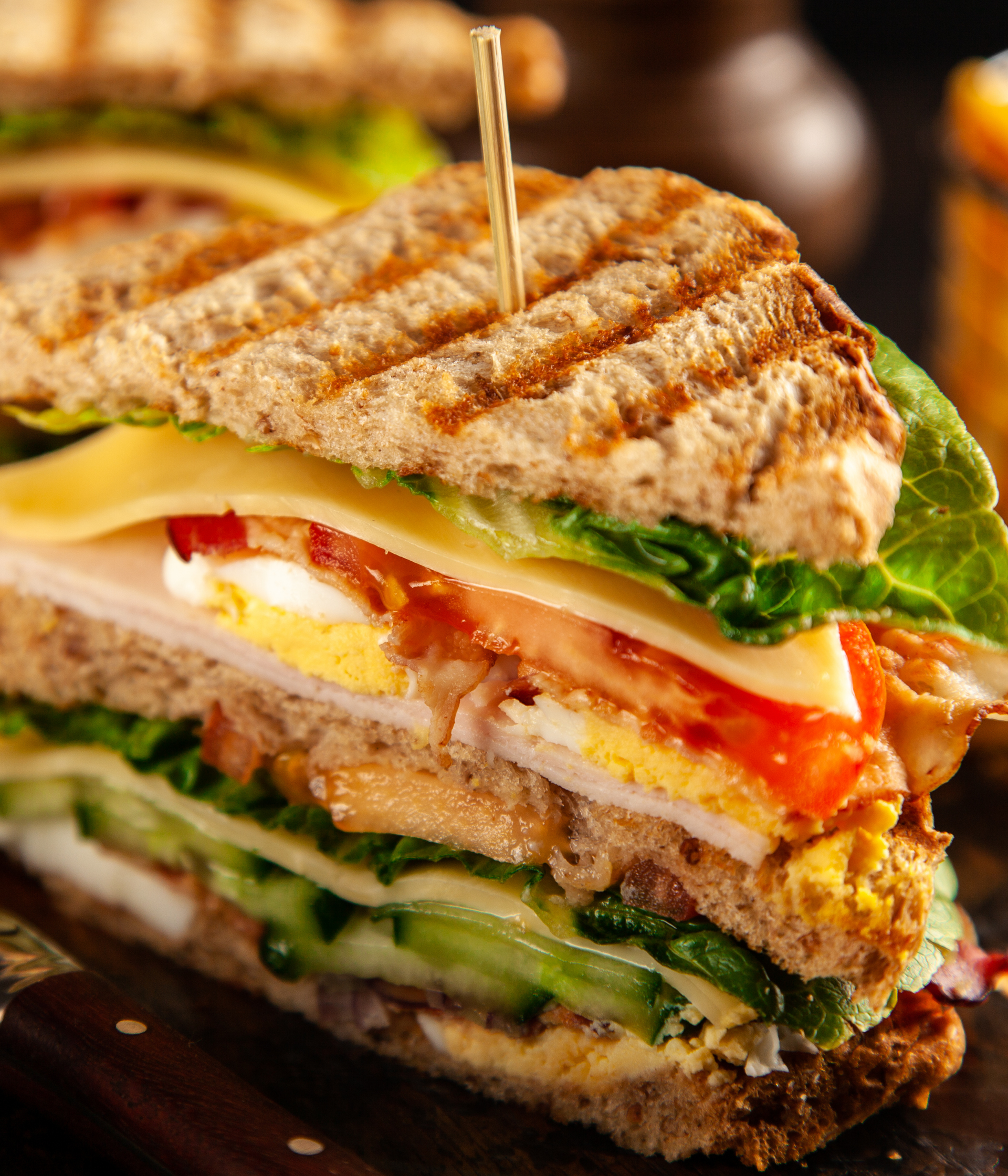 Grilled sandwich with cheese, tomato, lettuce, and bacon, held together with a toothpick.