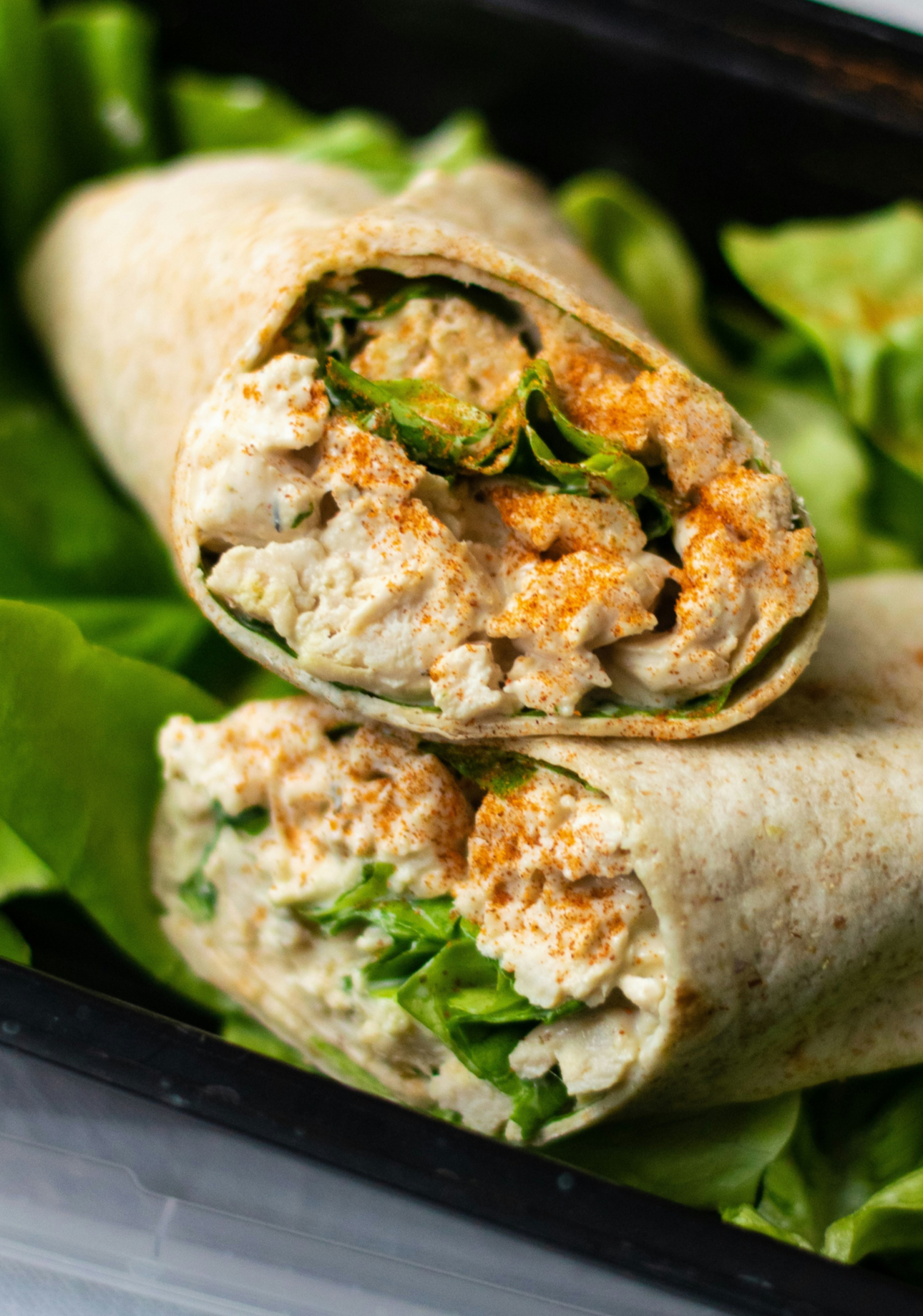 Two wrap sandwiches with lettuce on a black tray, one cut open to show the filling
