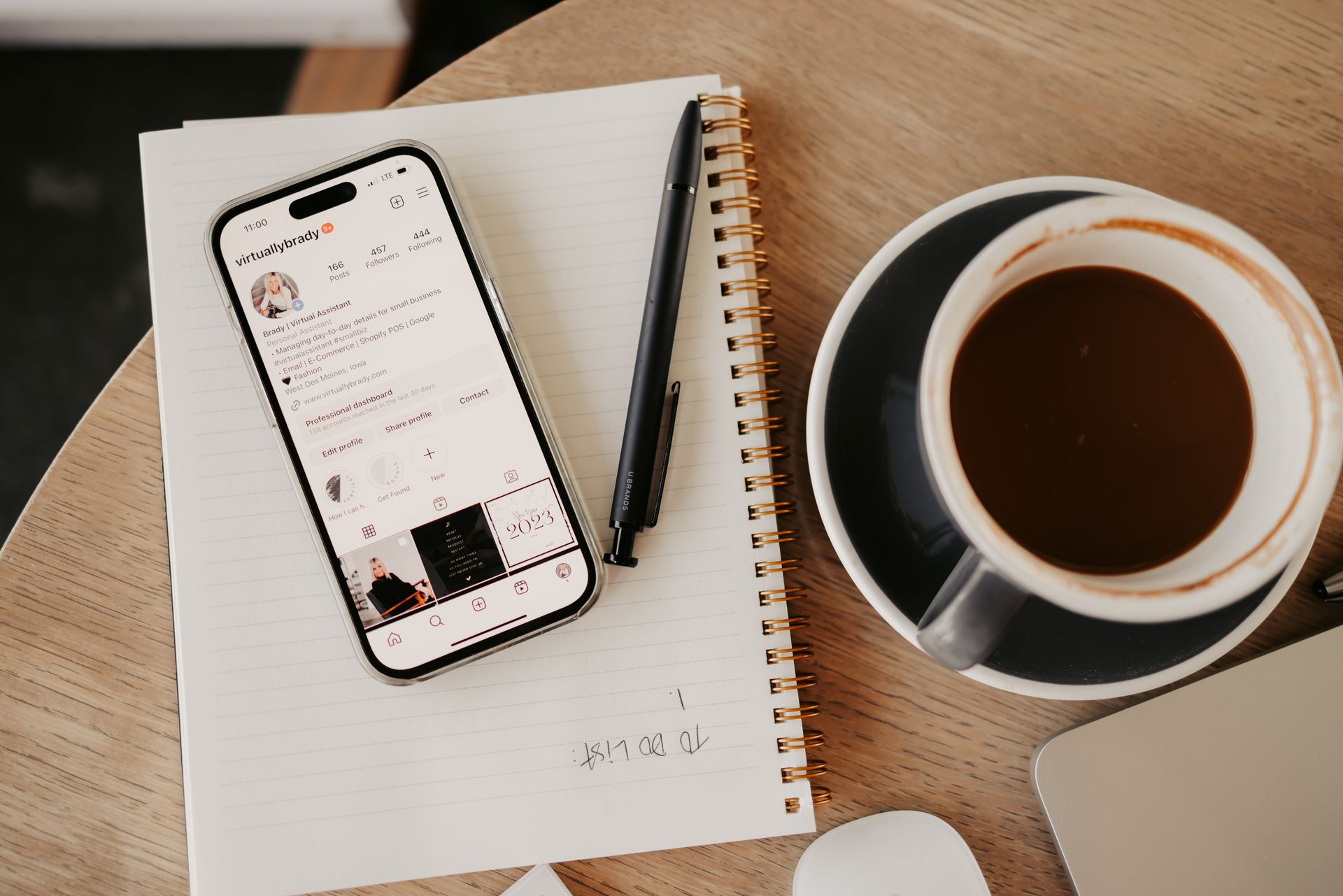 Smartphone displaying social media, pen, notepad, and coffee cup on a wooden table.