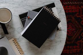 A stack of notebooks and a cup of coffee on a table.