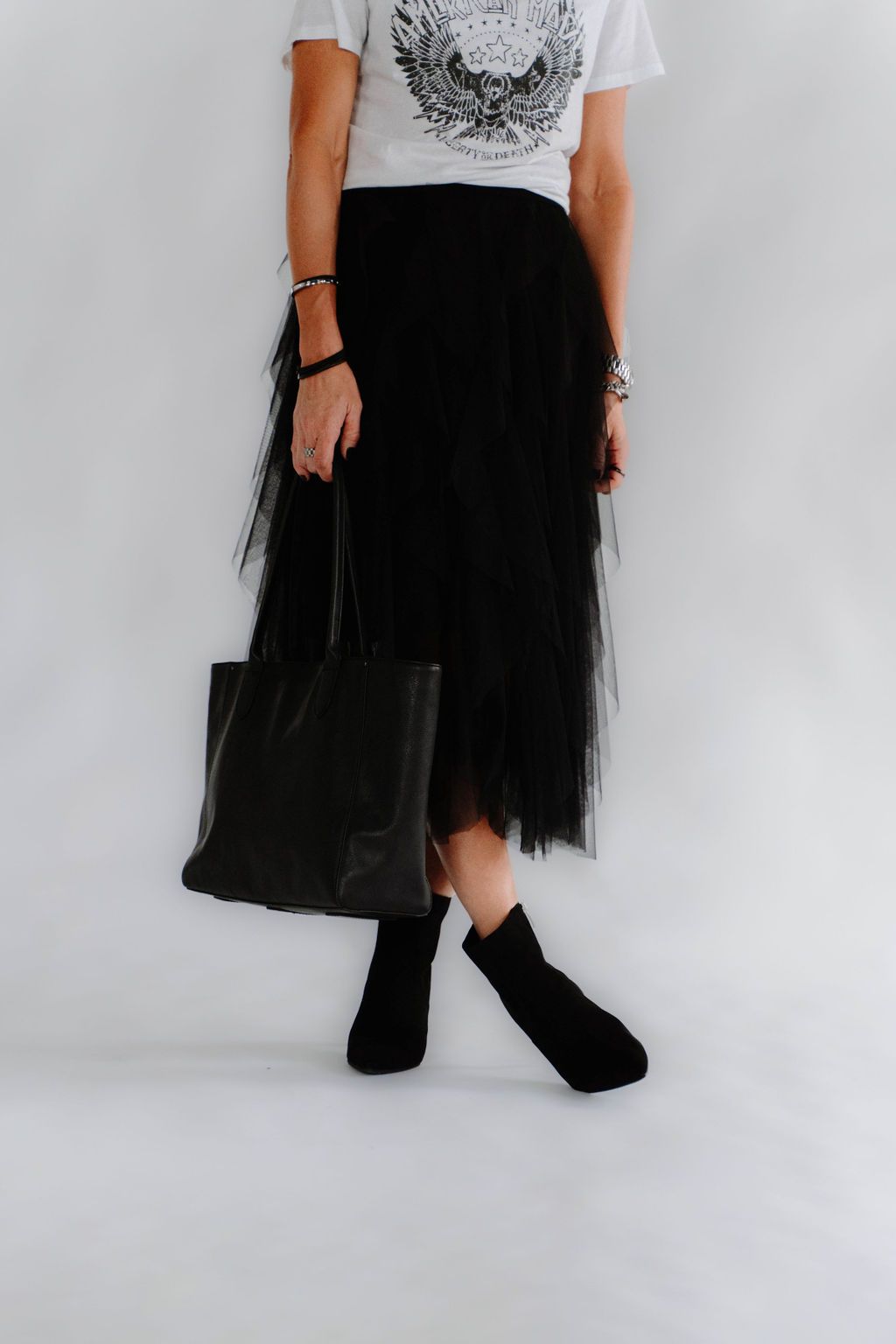 A woman wearing a white t-shirt and a black skirt is holding a black tote bag.