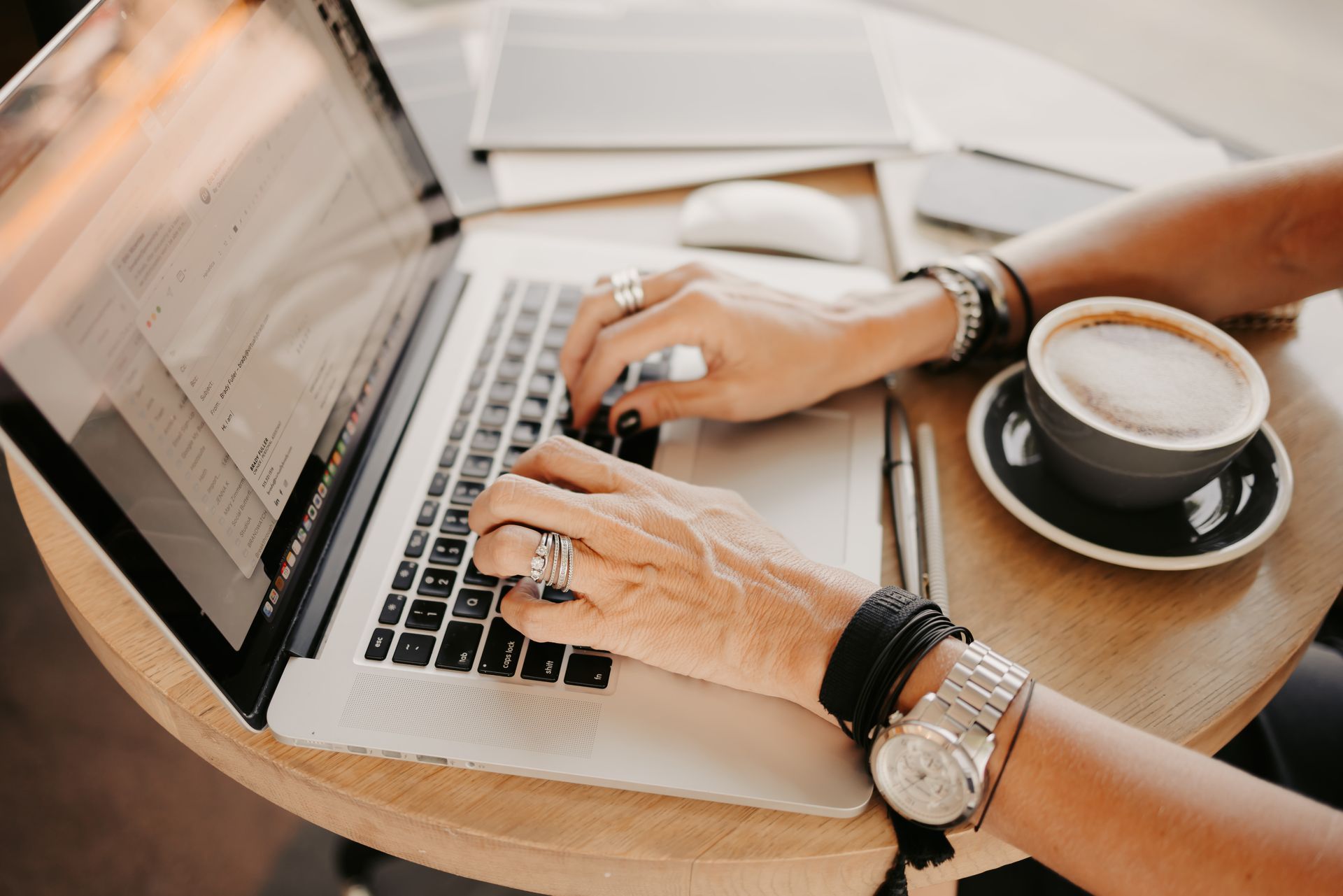 A woman is typing on a laptop computer while sitting at a table with a cup of coffee.