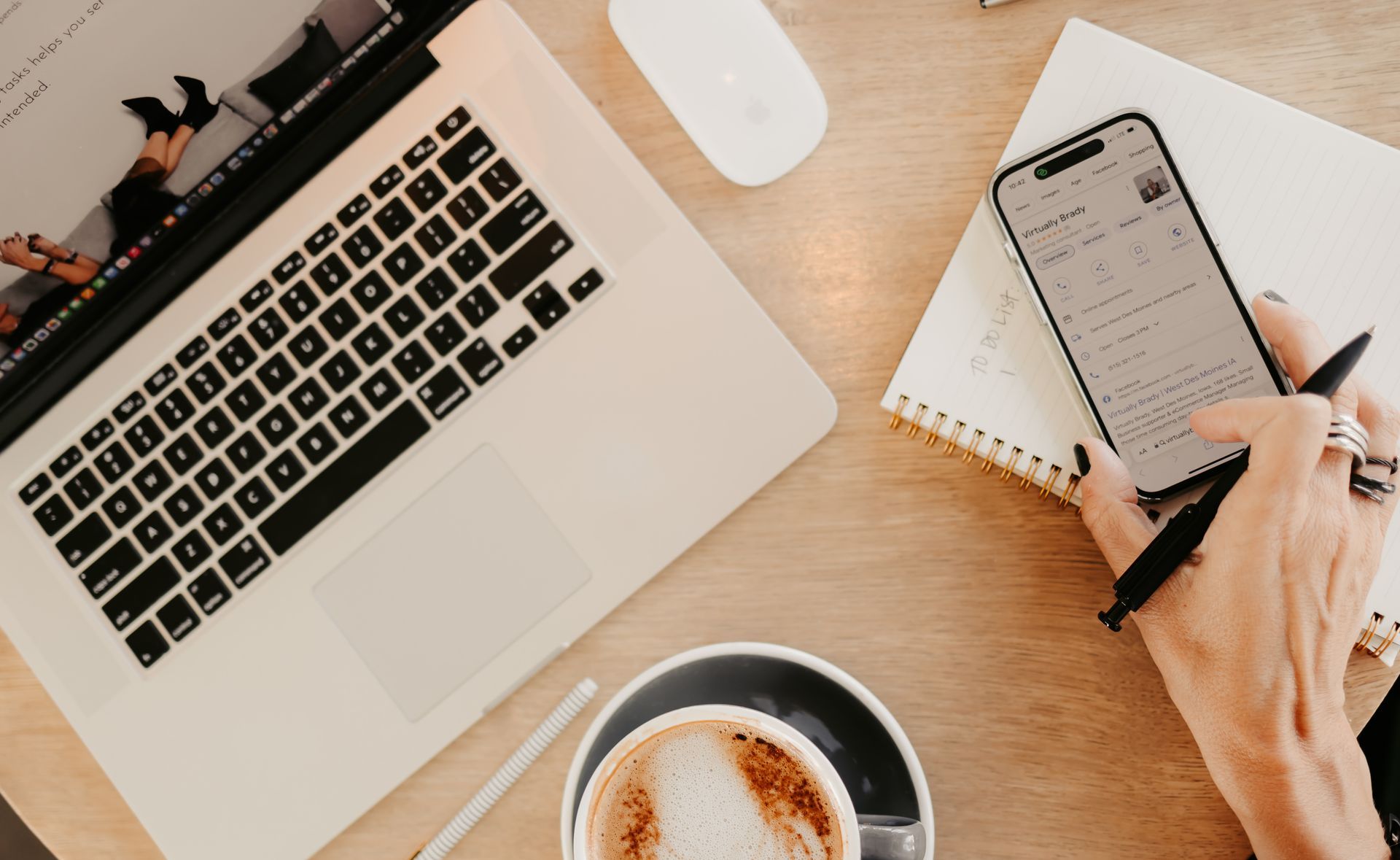 A person is using a cell phone next to a laptop and a cup of coffee.
