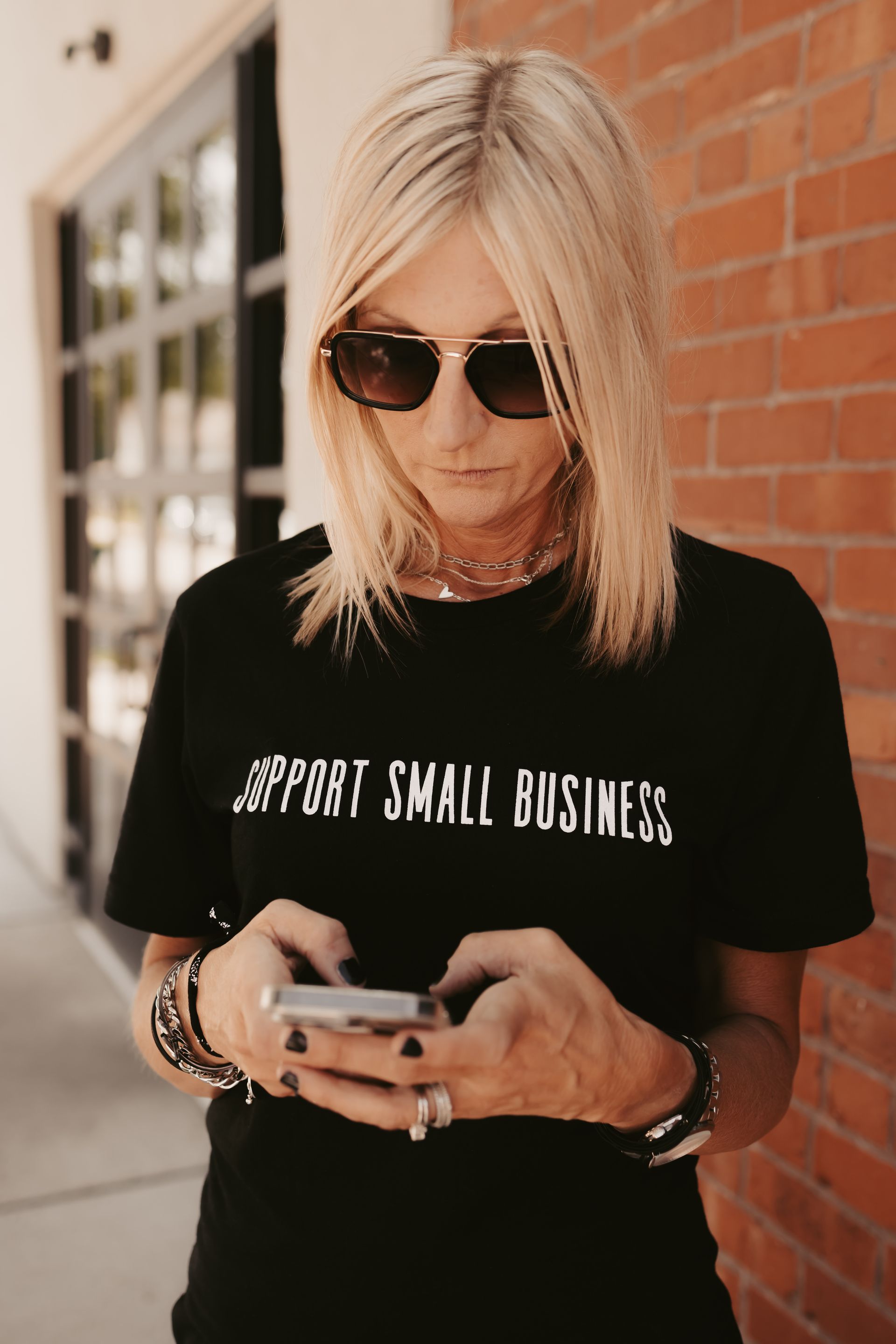 A woman wearing sunglasses and a black shirt is looking at her cell phone.