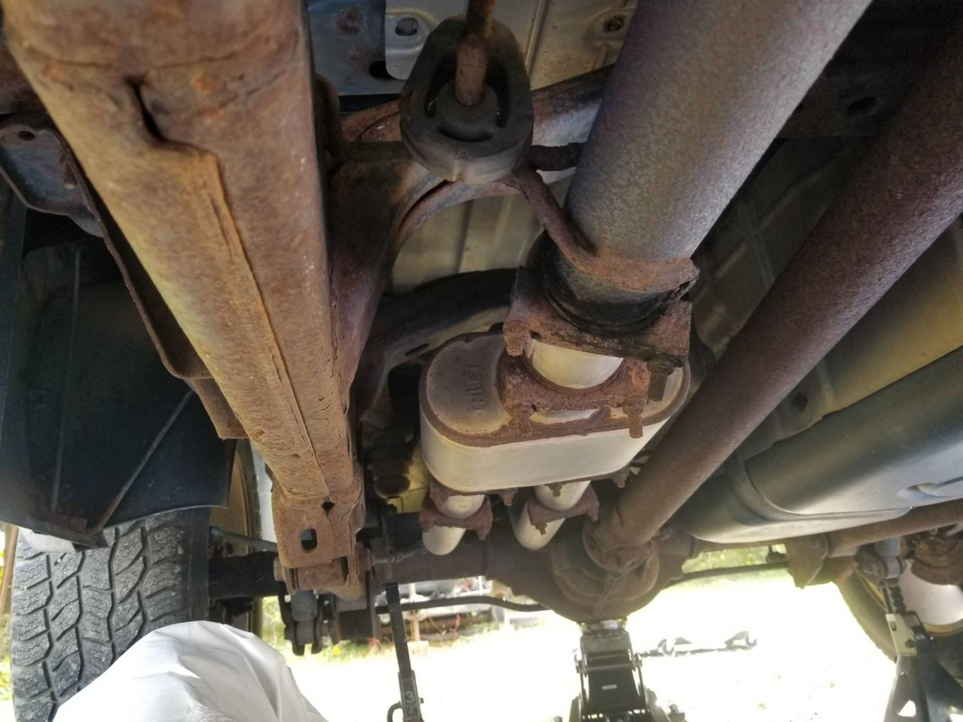 Undercarriage of a vehicle showing exhaust pipes, suspension parts, and rusted metal components