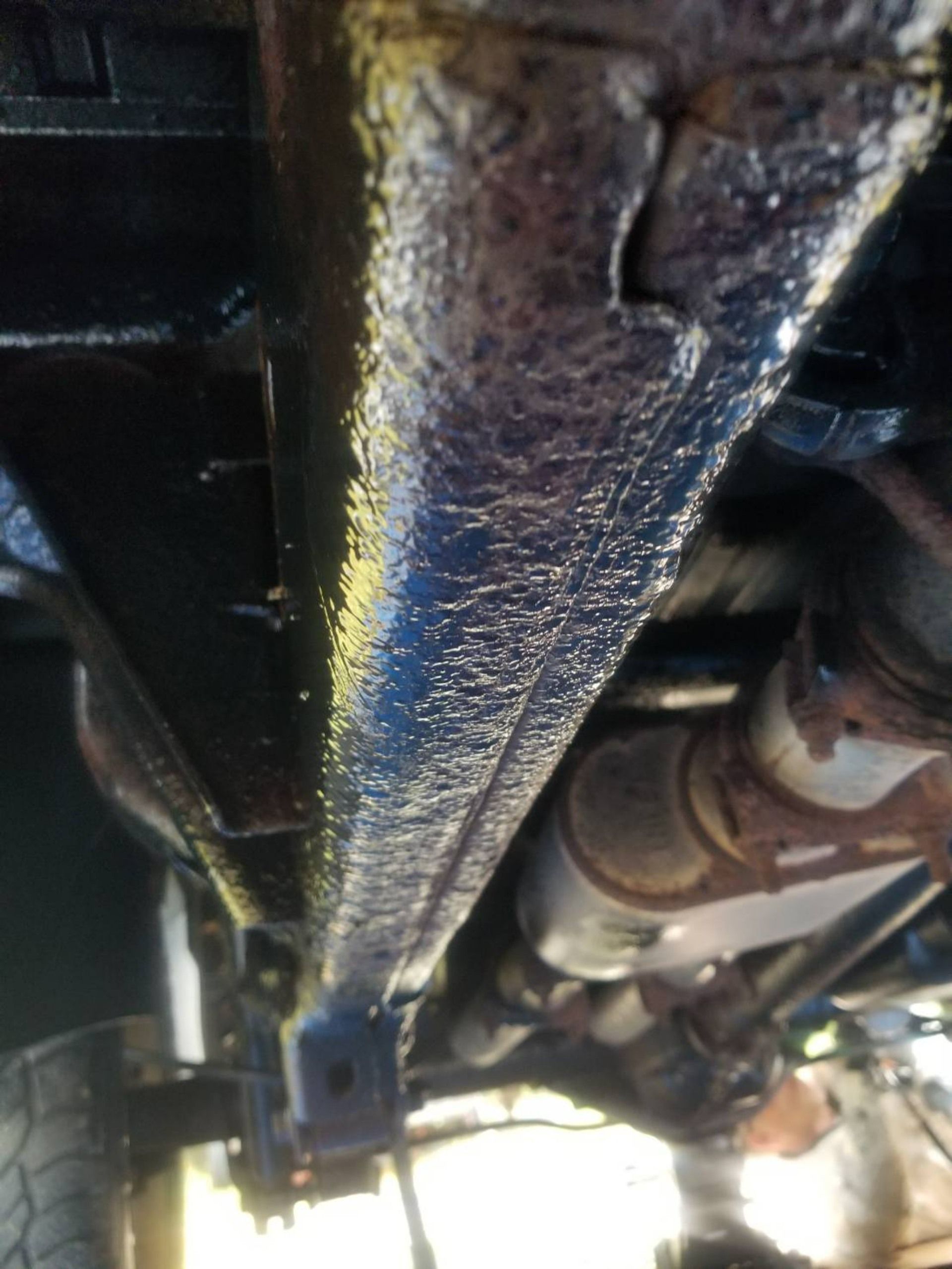 Undercarriage view of a vehicle, showing a rusty metal beam and exhaust components.