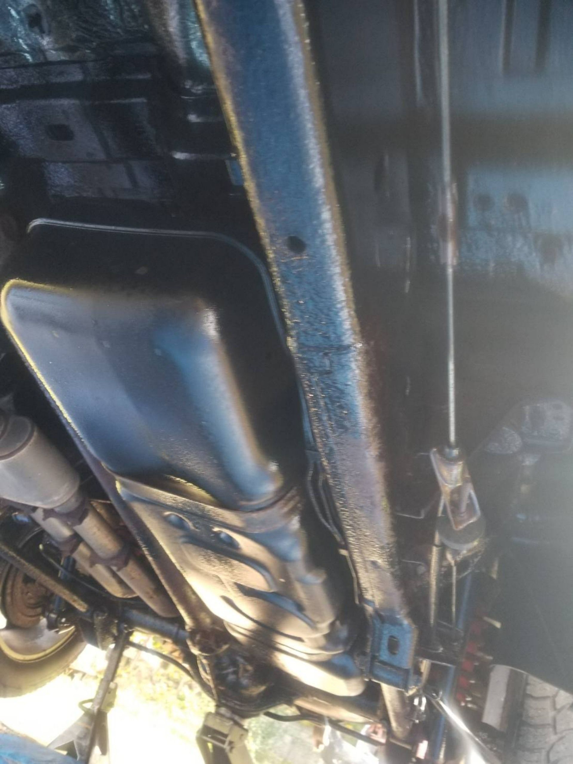 Underside of a vehicle showing metal frame, exhaust system, and blue structural beam on a lift