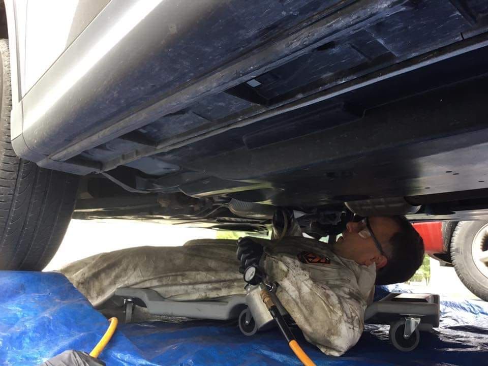 Mechanic lying under a car, using a flashlight in a garage, with tools nearby