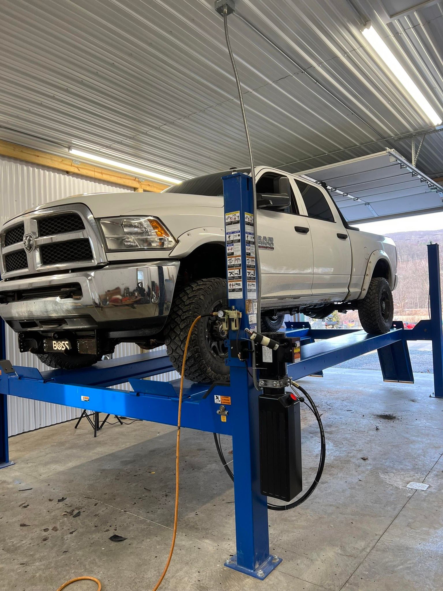 White pickup truck raised on a blue hydraulic lift in a garage workshop.