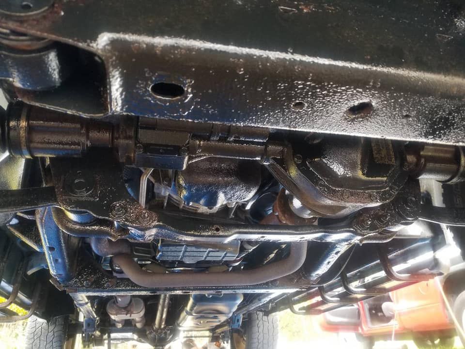 Undercarriage of a vehicle on a lift, showing exhaust pipes, suspension, and frame components.
