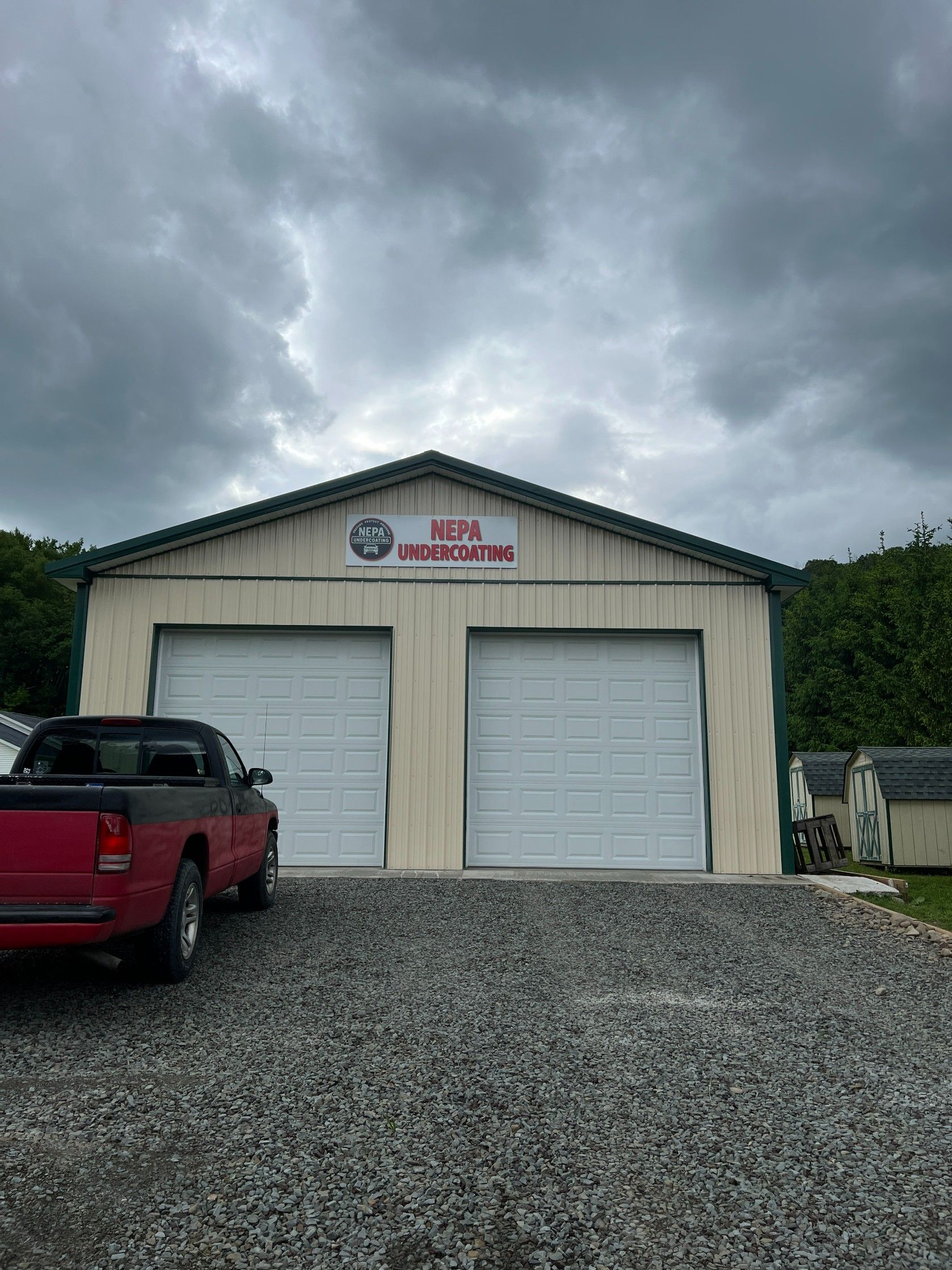 Red pickup truck in front of a beige garage with two white doors under a cloudy sky.
