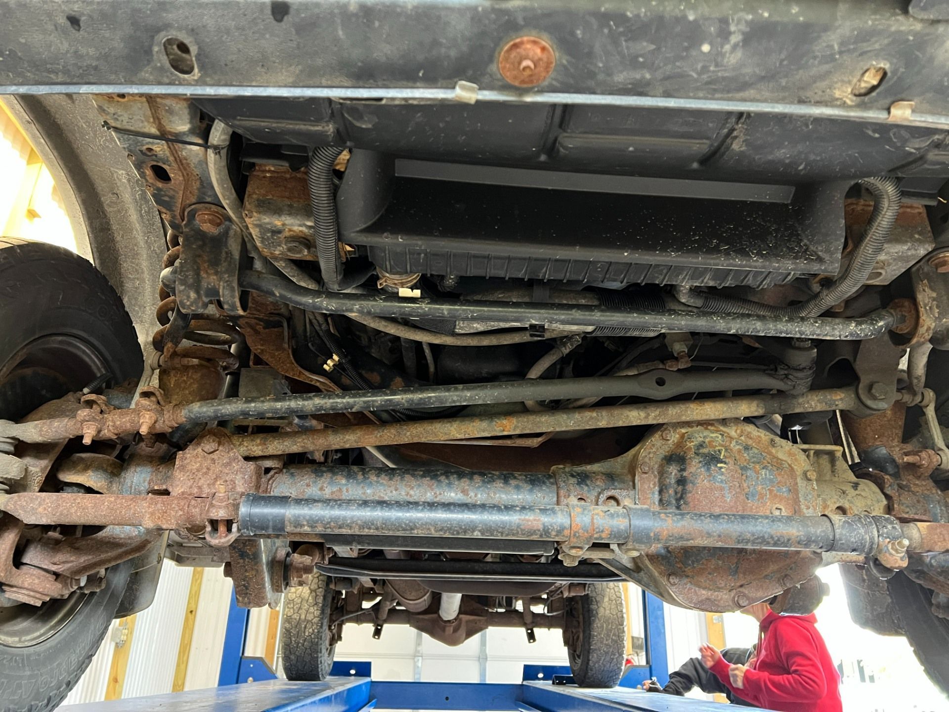 Undercarriage of a muddy vehicle, showing suspension and rear axle from below