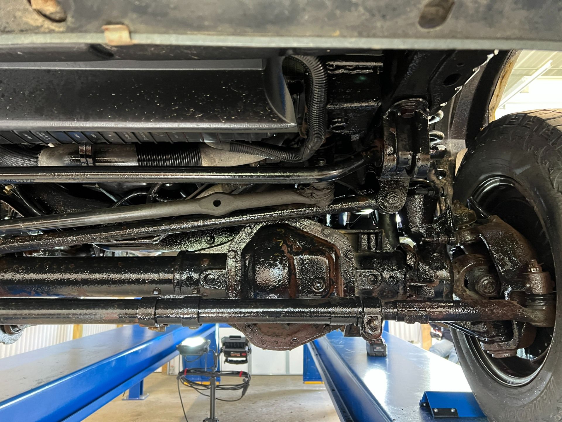 Undercarriage of a car on a lift, showing suspension and steering components with greasy mechanical parts.